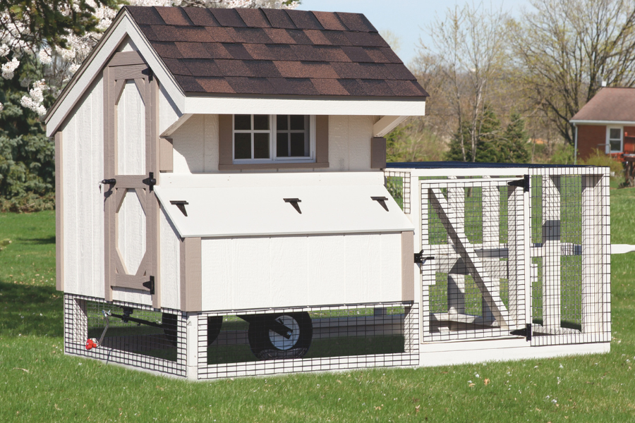 white and tan trimmed tractor coop with attached run and wheels in grass