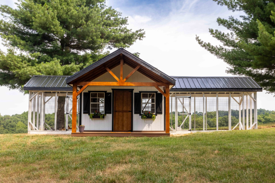 white and black trimmed combination chicken coops for sale in Bowling Green KY with attached runs of different lengths on either side featuring a front porch brown front door and two windows with black shutters and flower boxes beneath them and a black metal roof with solar panels