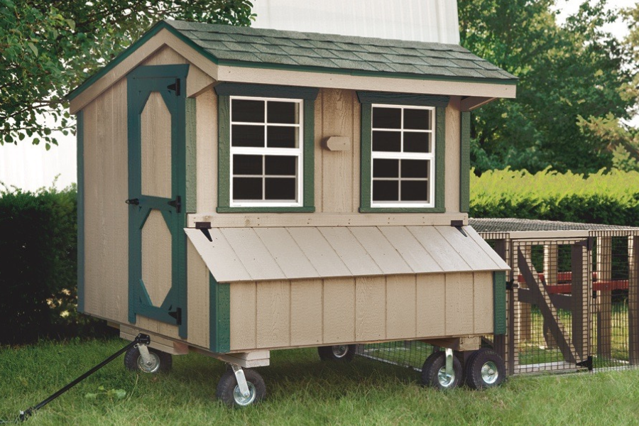 tan tractor chicken coop with dark green trim handle wheels and an attached run plus a greenish shingle roof