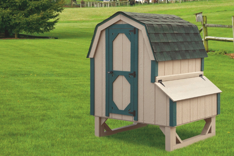 tan and dark green trimmed quaker chicken coop with green tinged shingle roof and egg collection box on side raised off of ground