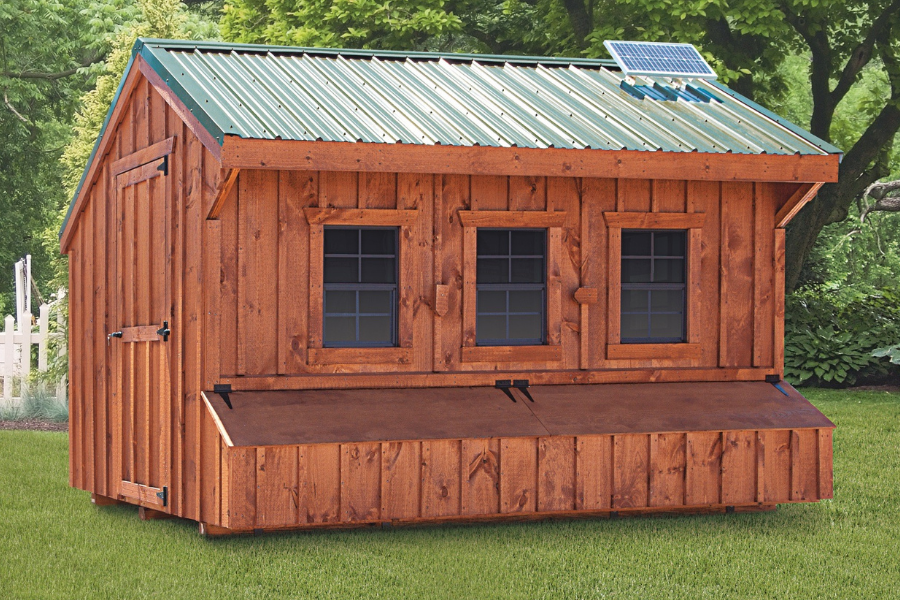wooden quaker chicken coops in Tennesse with green metal roof solar panel three windows and an egg collection box beneath