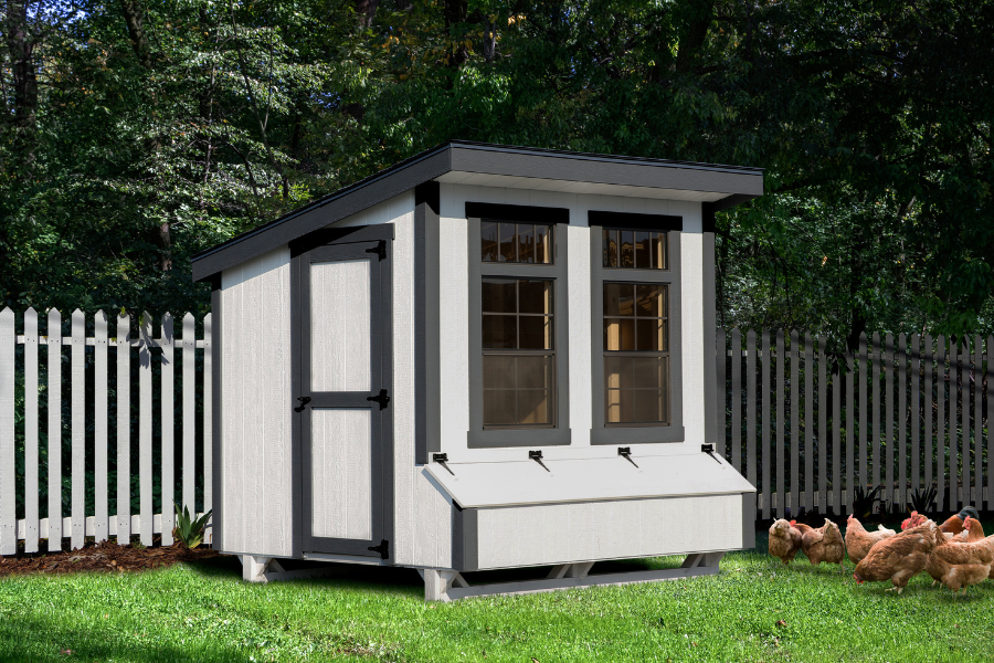 white and black trimmed lean to coop with two large front windows above egg collection box plus chickens grazing in grass in front of it