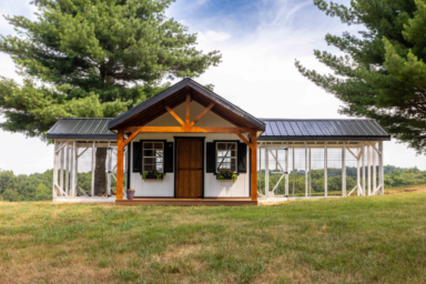 white chicken coop with front porch and two outdoor runs on either side and a black metal roof