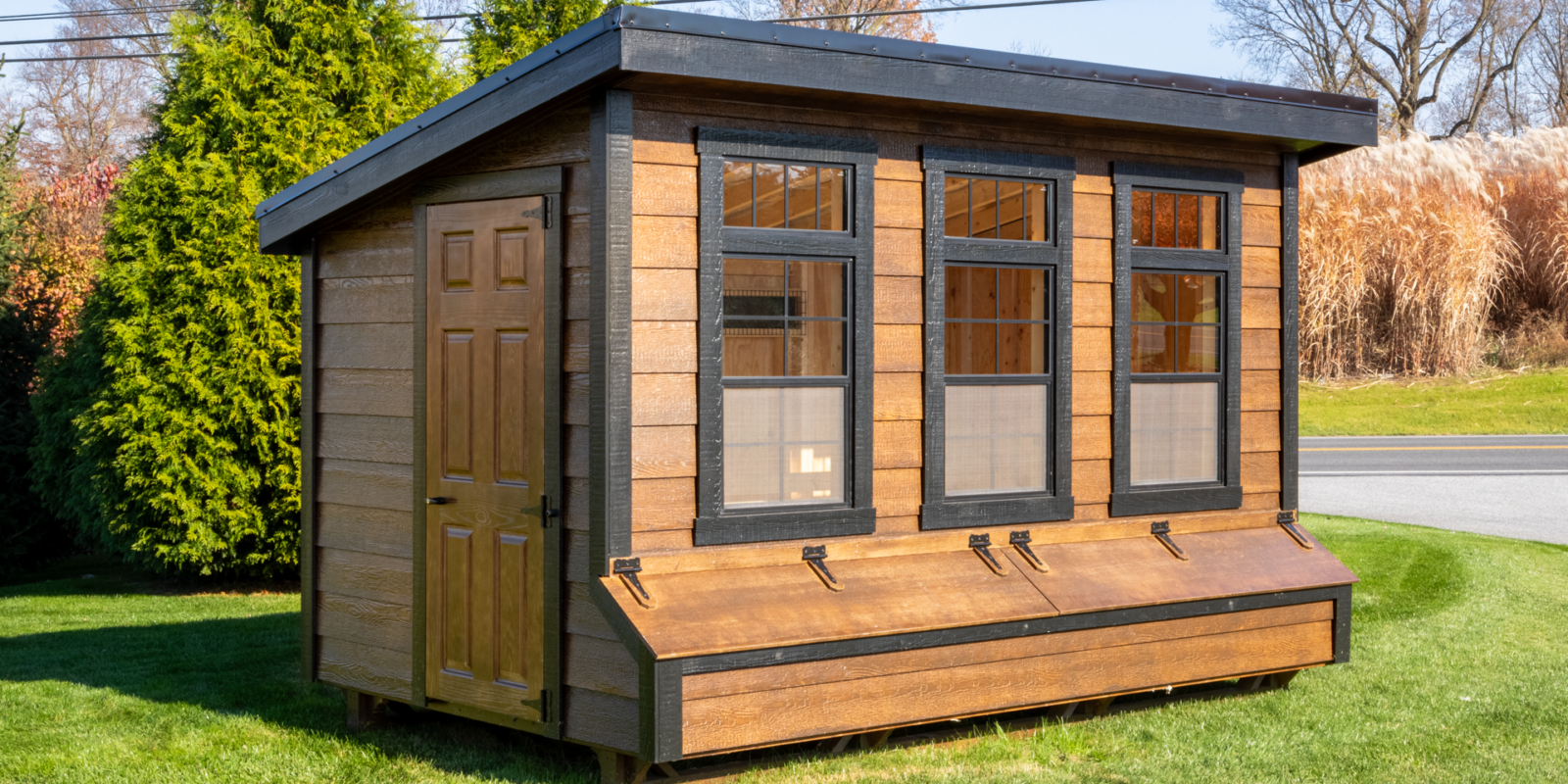 A Modern brown Lean-To chicken coop with three large windows and black trim.